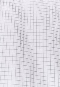 Tissu blanc avec un petit motif de grille grise, texture lisse, matière légère et couture uniforme partout.