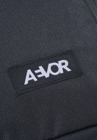 Schwarze Stofftasche mit strukturierter Oberfläche, die ein weiß gesticktes Etikett mit der Aufschrift "A=VOR" in einer fetten, modernen Schriftart zeigt.