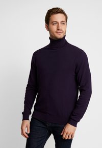 Lila Rollkragenpullover aus weichem Stoff, mit langen Ärmeln, gerippten Bündchen und Saum sowie einer figurbetonten Passform. Getragen mit dunklen Jeans.