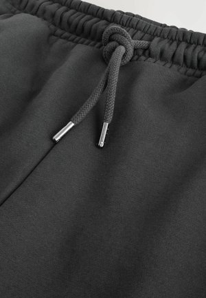 Mustad mustad püksid elastse vöökohaga ja sõlmimisega paelaga. Omab sileda kangatekstuuri ja hõbedast metallist detailidega paelade otstes.