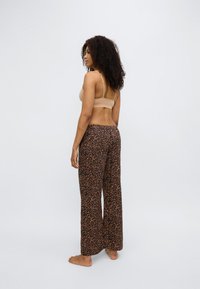 Pantalon large à motif léopard en tissu doux avec un motif texturé ; associé à un bralette couleur nude. Le mannequin est vu de dos, pieds nus.