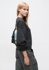 Μαύρο φούτερ με άνετη εφαρμογή, με έγχρωμη γραφική απεικόνιση παραλίας στην πλάτη. Ριμπ μανσέτες και τελείωμα, κατασκευασμένο από μαλακό ύφασμα.