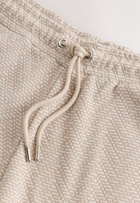 Bézs mintás zsinóros derékrész, szőtt textúrával és fém szemekkel. Lapos kötél, fém végződésekkel.