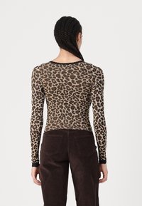 Top a maniche lunghe stampa leopardo in tessuto trasparente beige e nero, con un design attillato e bordi in pizzo, abbinato a pantaloni in corduroy marroni.