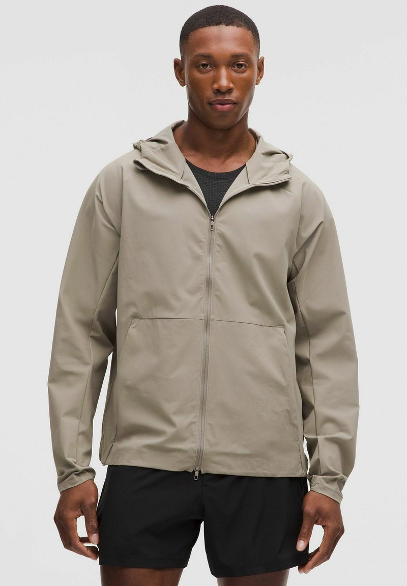 Leichtgewichtige beige Jacke mit Kapuze, Frontreißverschluss und Taschen. Das Design ist einfach und verfügt über eine glatte Textur im lässigen Stil.