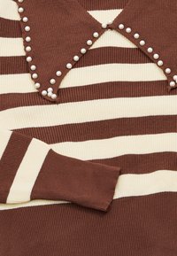 Braun- und cremefarbener gestreifter Pullover mit gerippter Textur, der einen großen Kragen mit weißen Perlen am Rand verziert hat.