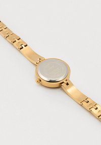 Gold wristwatch with a smooth metal band, round face, and a silver back. Features a crown and links in a shiny finish.