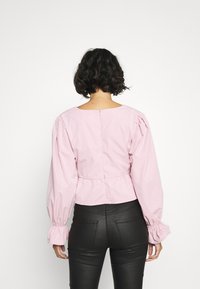 Blouse rose coupée avec des manches bouffantes et un col rond, dotée d'une taille peplum et d'une fermeture à boutons au dos.