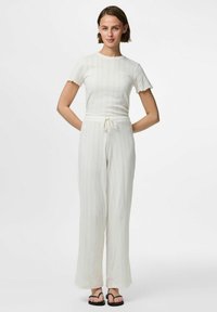 Top bianco a coste con maniche corte e arricciate abbinato a pantaloni bianchi larghi a vita alta, dotati di vita con stringa.