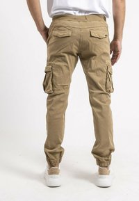 Pantalons cargo beiges avec des poignets élastiques, deux poches latérales et deux poches arrière. Fabriqués en coton, avec une coupe décontractée.