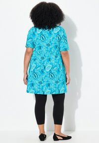 Turkusowa sukienka z krótkimi rękawami, zdobiona kwiecistym wzorem. Połączona z czarnymi legginsami i czarnymi balerinkami. Gładki materiał i luźny krój.