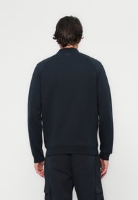 Sweatshirt bleu marine avec des manches raglan, des poignets et un ourlet côtelés, présentant une texture lisse et un design minimalist au niveau de l'encolure dans le dos.