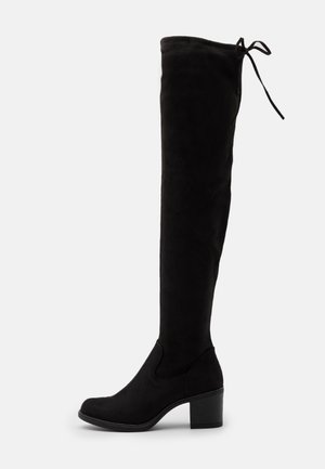 Botte noire en daim au-dessus du genou avec talon bloc et détail à lacets en haut, vue de profil sur fond blanc.