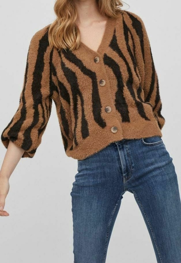 Femme portant un cardigan marron duveteux avec des rayures zébrées noires et des boutons, associée à un jean bleu taille haute.