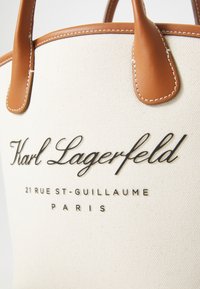 Lærredstotte taske med brune læderhåndtag, prydet med præget sort tekst: "Karl Lagerfeld," "21 RUE ST-GUILLAUME," og "PARIS."