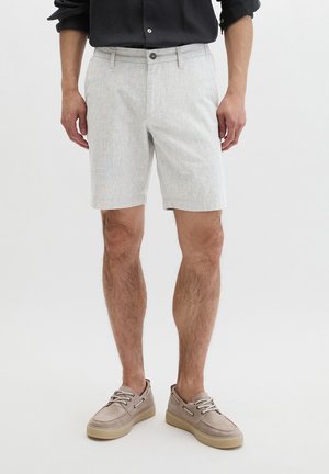 Man die lichtgrijze knie-lange korte broek, beige casual veterschoenen en een zwart overhemd met opgerolde mouwen draagt.