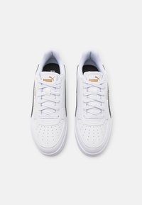 Baskets en cuir blanc avec des accents noirs, bout rond, design perforé à l'avant, lacets plats, et logo doré sur la languette.