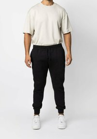 Ljusgrå t-shirt med kort ärm i kombination med svarta sweatpants med elastiskt midjeband och muddar, kompletterad med vita sneakers.