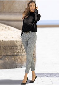 Zwarte geribbelde trui gecombineerd met grijs geruit broek. De broek heeft een strakke snit en een zwarte riem met gouden hardware. Zwarte hakken maken de look compleet.