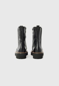 Botine negre din piele până la glezne cu finisaj neted, vârful rotunjit și talpă din cauciuc masiv. Au fermoar pe lateral și o bandă de tragere la spate.