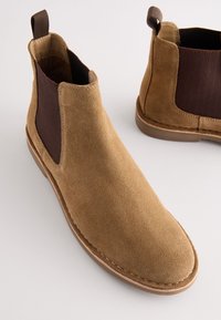 Bruine suède Chelsea-laarzen met elastische zijkanten, aantreklipje en rubberen buitenzool. Gladde textuur, ronde neus en minimale stikdetails.