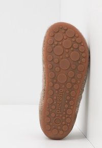 Semelle en feutre marron avec des motifs de grip circulaires et un logo en relief. Texture douce, design léger et forme arrondie pour un confort optimal.