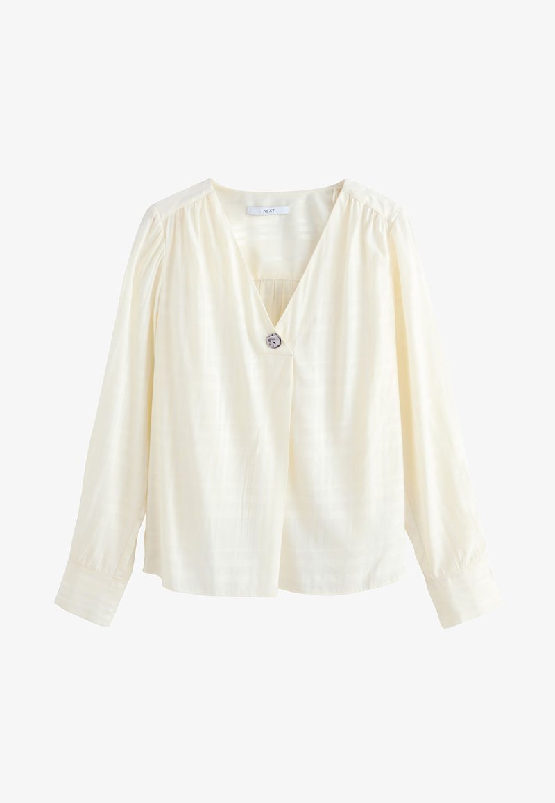 Krémová blúzka s dlhými rukávmi a výstrihom do V, s jedným dekoratívnym gombíkom pod výstrihom a jemnými skladmi na pleciach a manžetách.