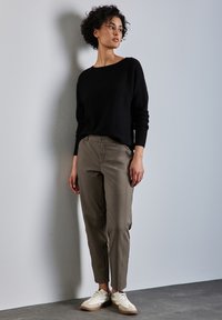 Pull en maille noire, pantalon vert olive et baskets blanches. Le pull a un col large ; le pantalon a une coupe ajustée et fuselée avec des poches avant visibles.