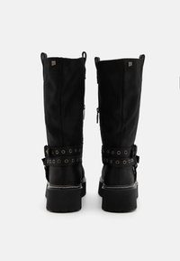 Black knee-high boots made of soft fabric, featuring a strap with metal eyelets, chunky rubber soles, and back zipper closures.