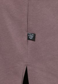 Indumento in cotone bordeaux con uno spacco laterale e un piccolo etichetta nera con testo bianco. Texture liscia, design aderente.