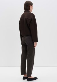 Sweatshirt marron court avec col montant, associé à un pantalon vert foncé à coupe droite et des chaussures plates noires. Texture du tissu lisse.