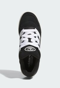 Zapatilla negra con cordones blancos y tres rayas blancas. Presenta un upper texturizado, un acolchado en el cuello y un logo circular en la lengüeta.