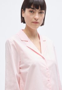 Chemise rose clair à boutons, en tissu lisse, dotée d'un col à revers et de manches longues, avec une coupe décontractée et des boutons délicats.