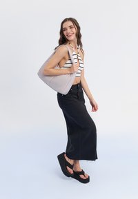 Grå quiltad handväska med rundad form, kombinerad med en randig crop top och svart maxikjol. Platta plattform flip-flops fulländar looken.