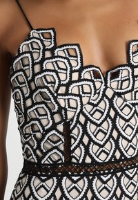 Svart och vit broderad klänning med en scalloped halsringning och intrikata geometriska mönster på en genomskinlig bas med en nätmidja.