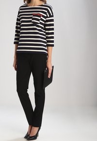 Top a maniche lunghe a righe blu navy e crema con taschino sul petto. Abbinato a pantaloni neri slim e scarpe con tacco nero, mentre tiene una pochette.