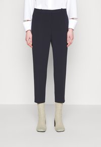 Pantalones sastre azul marino con corte slim, textura suave, largo recortado y dos bolsillos delanteros, combinados con botas beige hasta el tobillo.