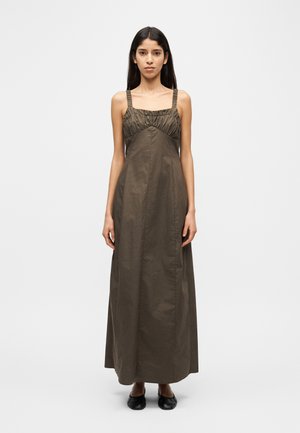 Õlivihreast puuvillast maksikleit, millel on kogutud ülakeha, sirge siluett ja reguleeritavad rihmad; komplekteeritud mustade kingadega.