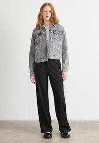 Lichtgrijze denimjas met een cropped design, voorzien van een knoopsluiting, borstzakken en contrasterende stiksels, gecombineerd met zwarte wijde broek.