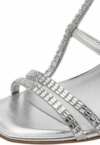 Silver metallic sandals featuring crisscross straps adorned with square rhinestones on the upper. Smooth texture and elegant design.