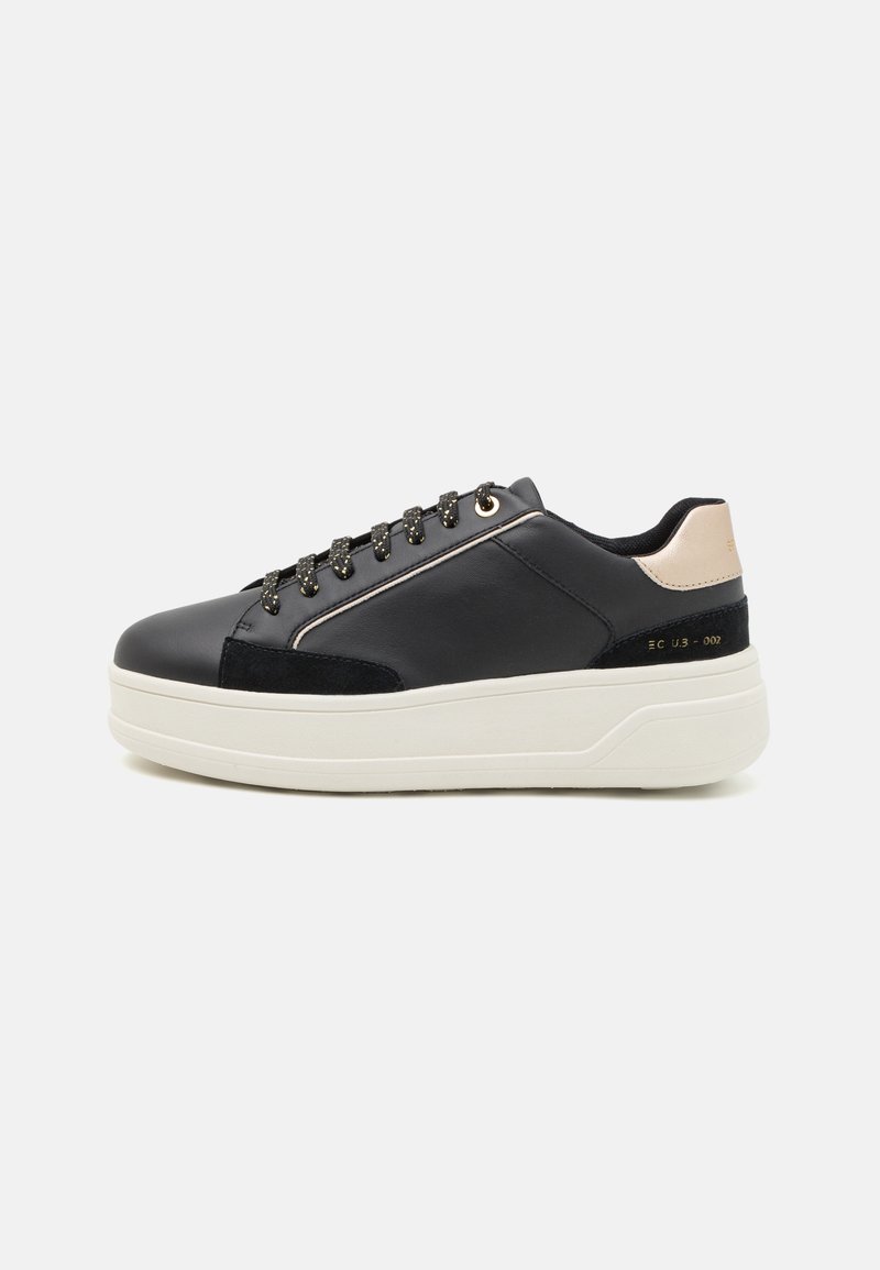 Sneaker in pelle nera con suola piatta bianca, accentuata da occhielli e lacci dorati, caratterizzata da un pannello in suede nero e un tacco beige chiaro.