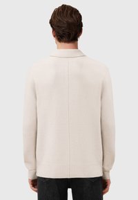 Pull en maille beige clair avec col, poignets côtelés et ourlet droit. La texture est douce avec un design dos minimalement détaillé.