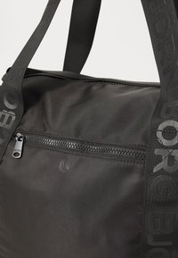 Svart nylonveske med blank glidelås og store håndtak, prydet med preget logo. Jevn tekstur med en subtil glans på overflaten.