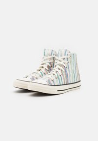 Zapatillas altas de tela blanca con franjas verticales de colores. Cuentan con cordones blancos, suelas de goma gris y líneas de acento negras.