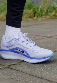 Sapatilha de corrida leve em branco e azul, com parte superior em malha respirável, sola almofadada e detalhes texturizados.