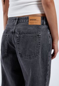 Gray denim jeans feature a straight-leg design, accented with two back pockets and a tan leather brand patch on the waistband.