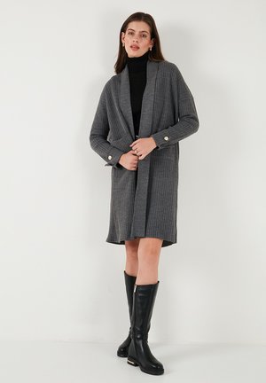 Gray ribbed cardigan with long sleeves, open front, and gold button details. Paired with a slim black turtleneck and knee-high black boots.