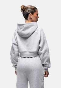 Felpa grigia corta con tasca frontale, maniche oversized e cappuccio con cordini. Tessuto morbido e strutturato con una vestibilità rilassata.