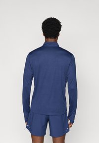 Σκούρο μπλε μακρυμάνικο πουκάμισο polo με γιακά, μαλακή υφή και ίσια γραμμή. Φοριέται με αντίστοιχα σορτς, με ελάχιστη ορατή σήμανση.