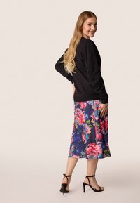 Zwarte lange mouwen sweatshirt gecombineerd met een bloemenprint rok in blauw, roze en groen. Model draagt zwarte strappy hakken.